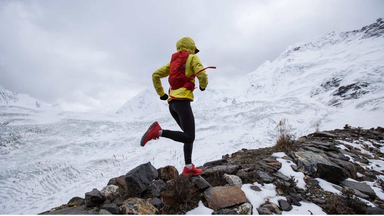 A person running through the snow and rocks on a mountainside 