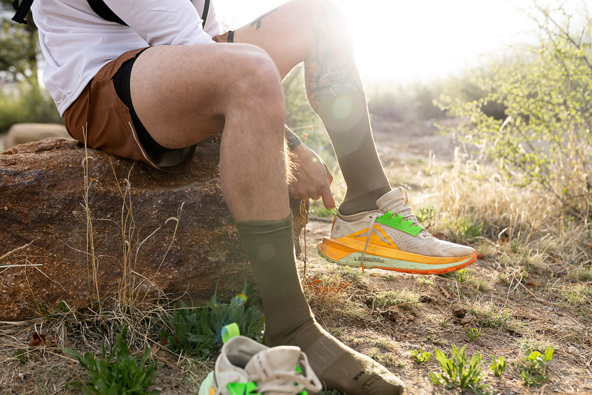 A person sitting on a rock and putting on Wrightsocks Single Layer Crew Socks.