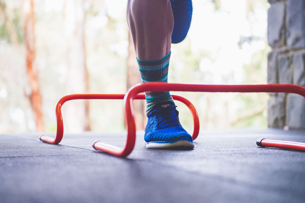 Person jumping over a red hurdle on a path with blurred background.