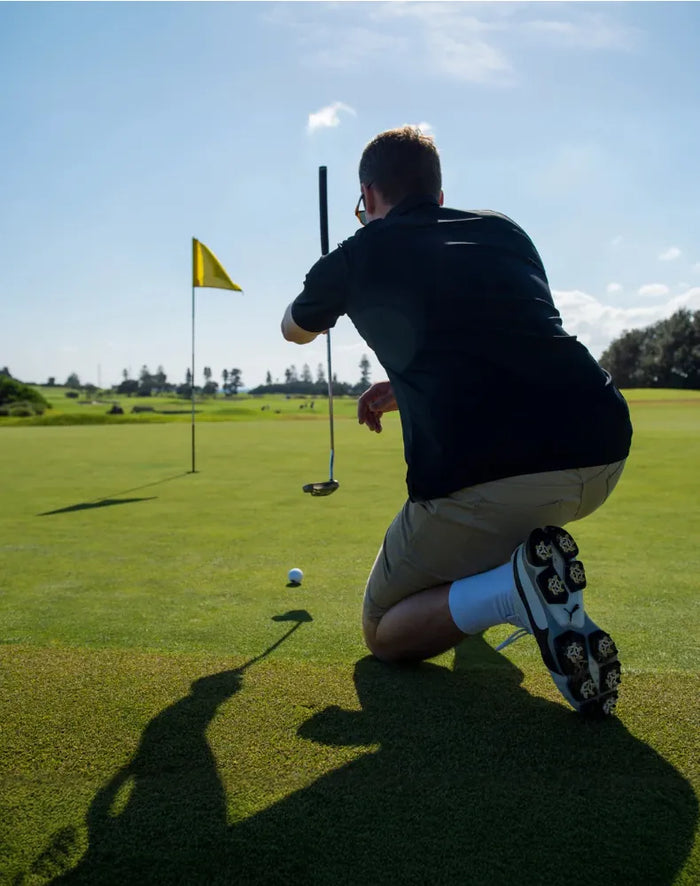 Person on a golf course preparing to putt with a flag in the background.
