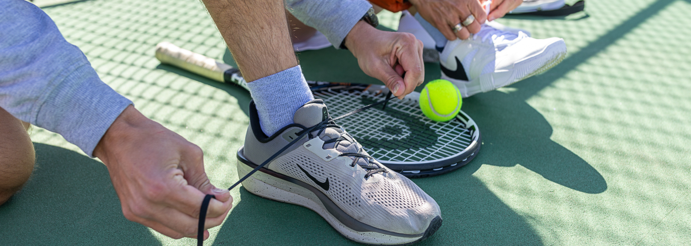A person tying their shoes on a tennis court and wearing Wrightsock Single Layer Quarter Socks.