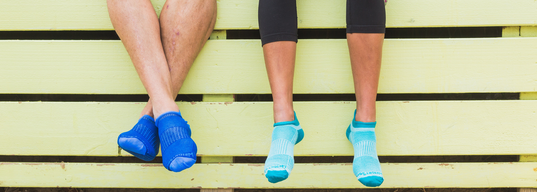 A pair of people sitting on a fence and wearing Wrightsock Double Layer Tab Socks.