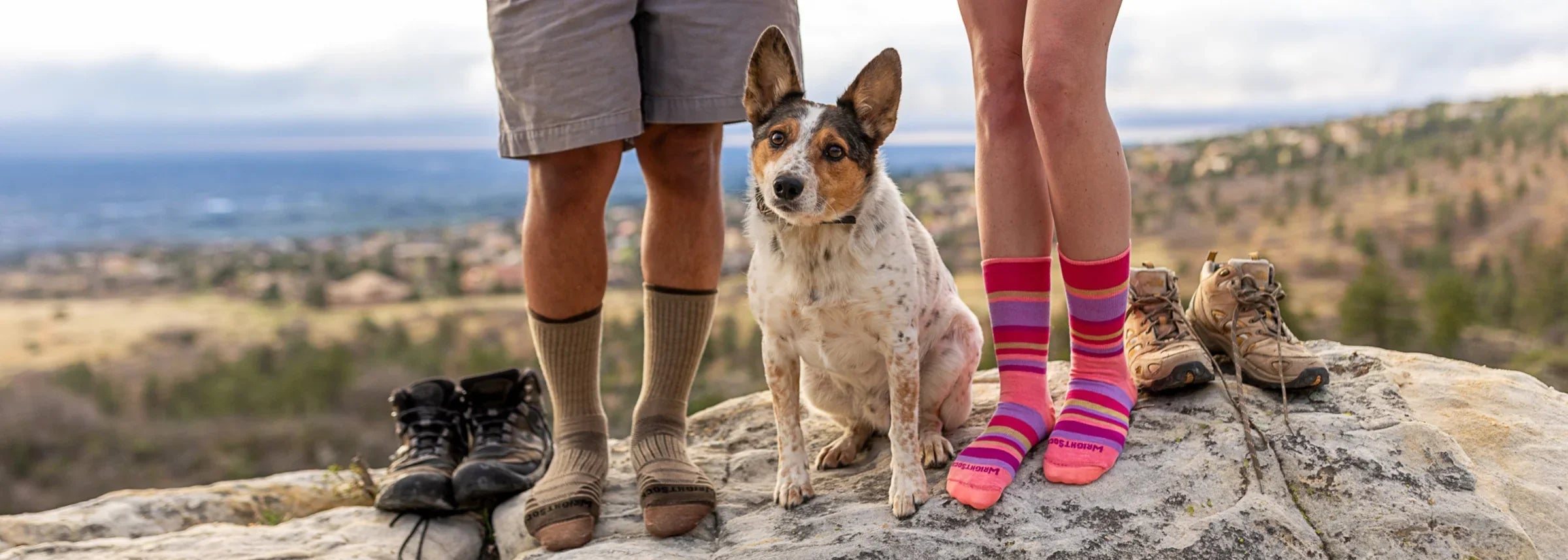 Two people standing on a rock with a dog and wearing Wrightsock Double Layer Crew Socks.