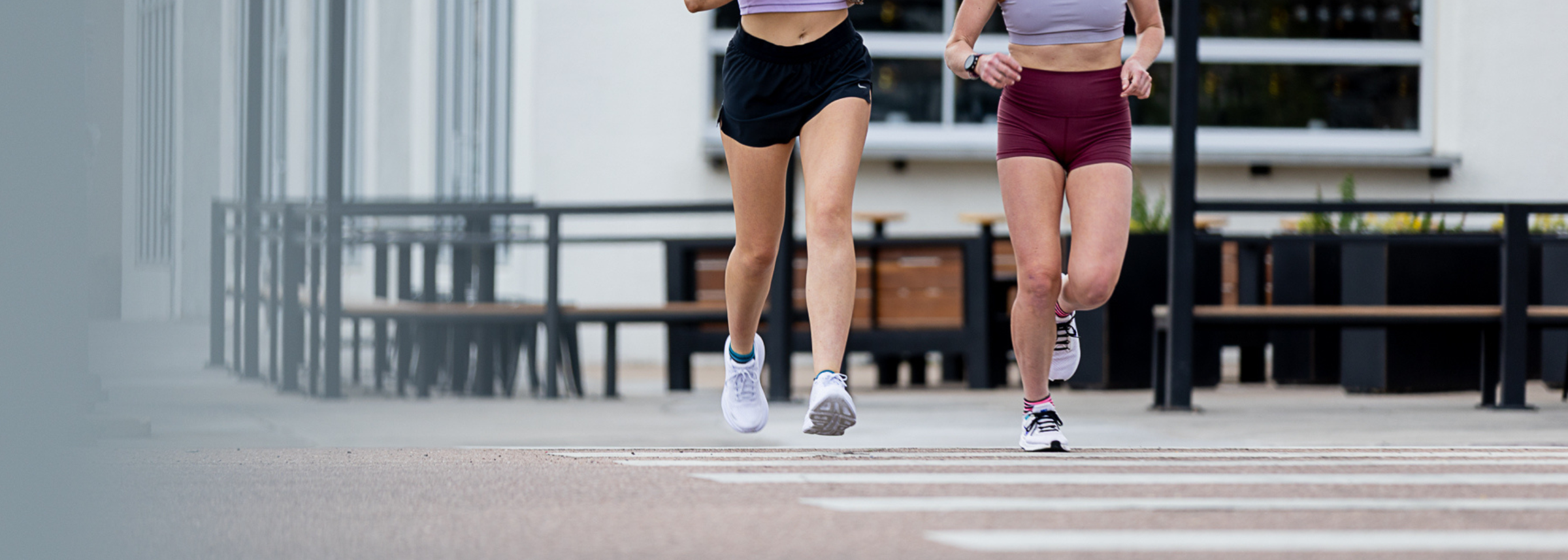 Two people running on a city street with buildings and benches in the background.